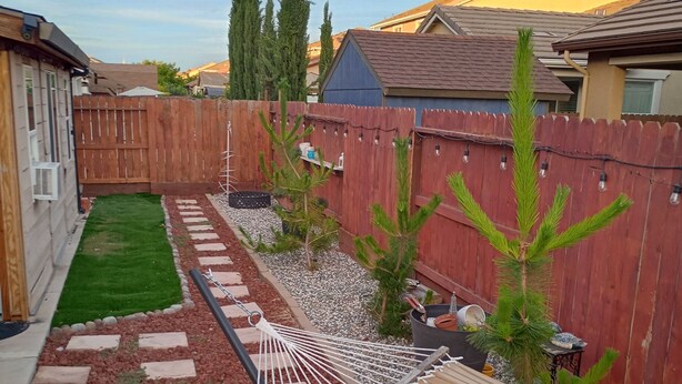 Un jardin avec un hamac, une petite pelouse, une clôture en bois et un espace patio.