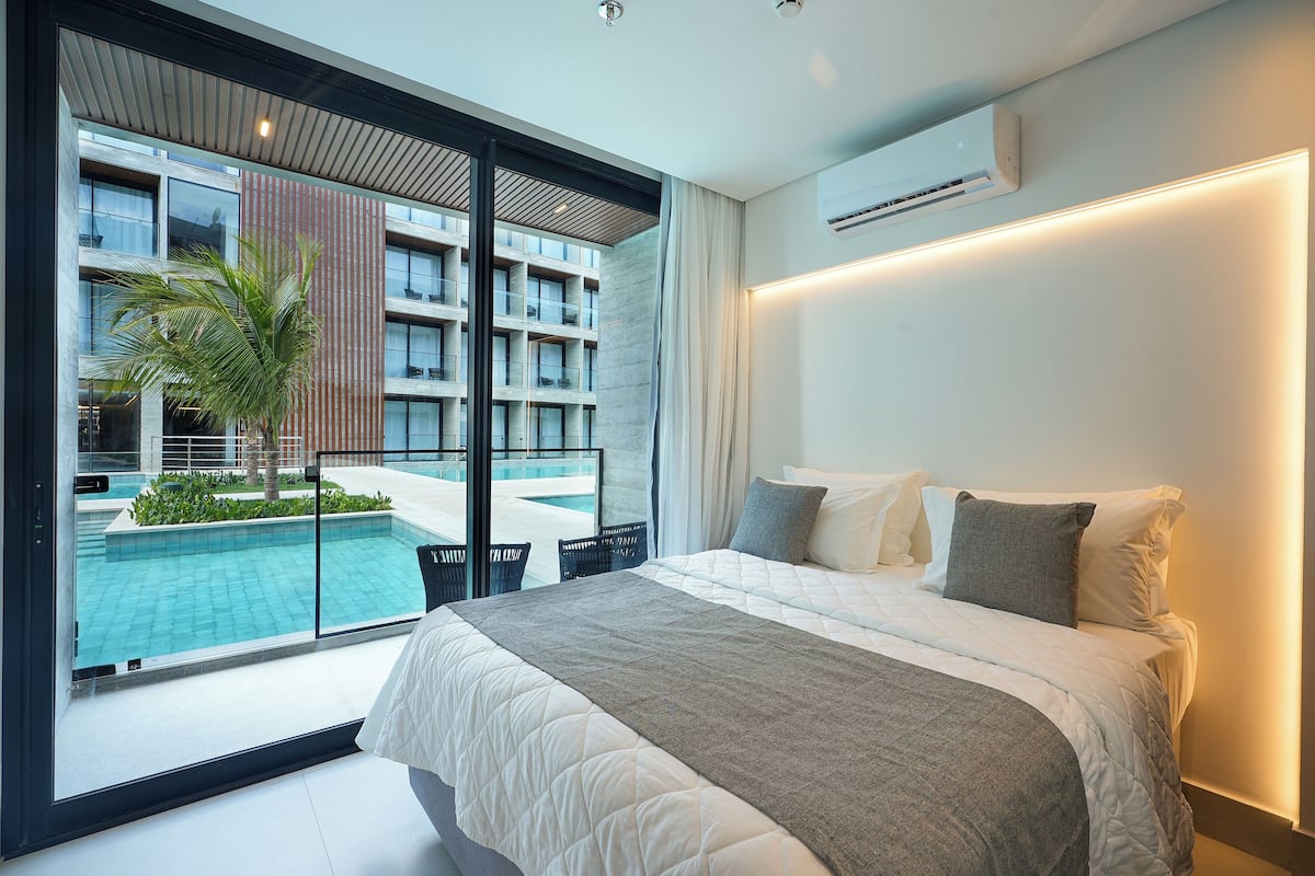 Une chambre d’hôtel moderne avec un grand lit, une vue sur une piscine et un climatiseur fixé au mur.
