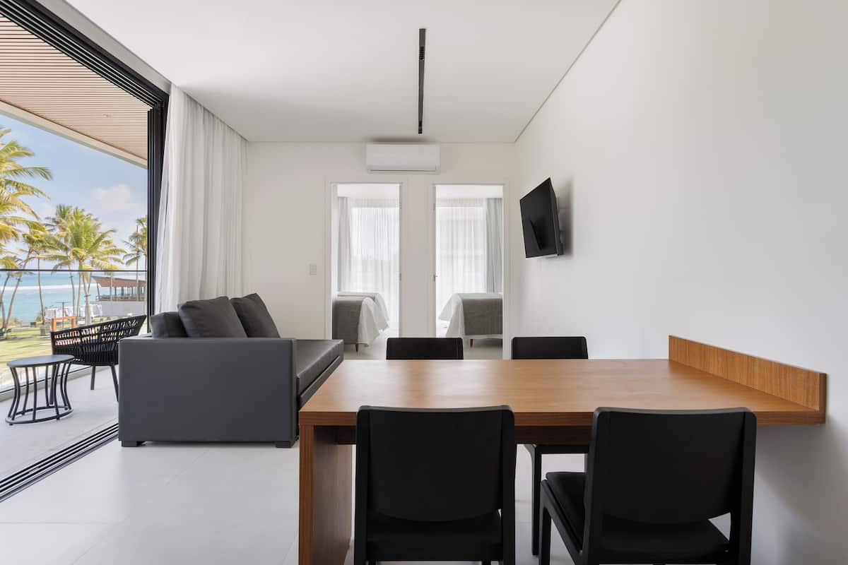 Un salon moderne avec une table à manger en bois, des chaises noires, un canapé gris et un téléviseur fixé au mur.