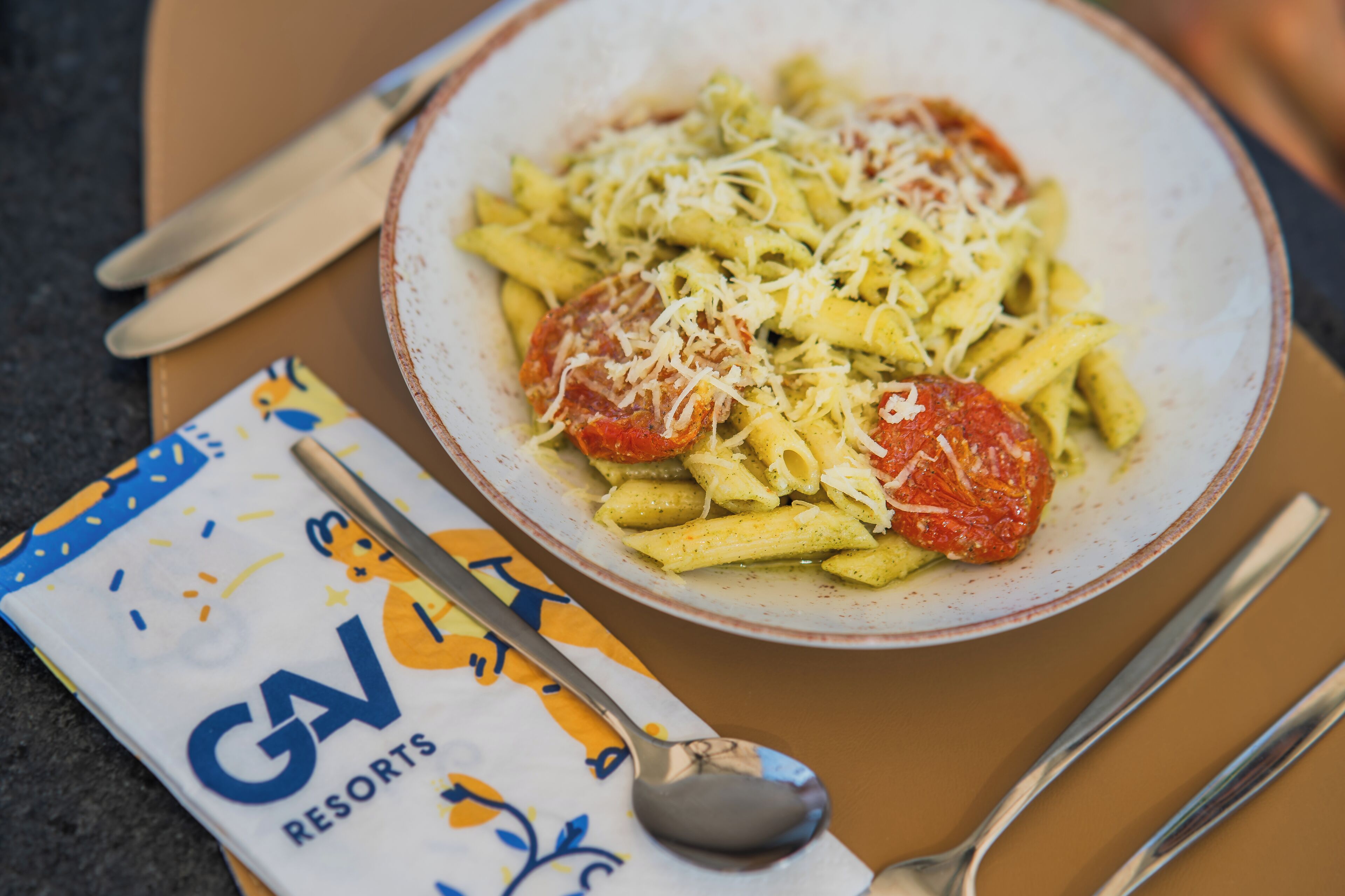 A plate of pasta with tomato sauce and cheese, a spoon, and a napkin with a printed design.