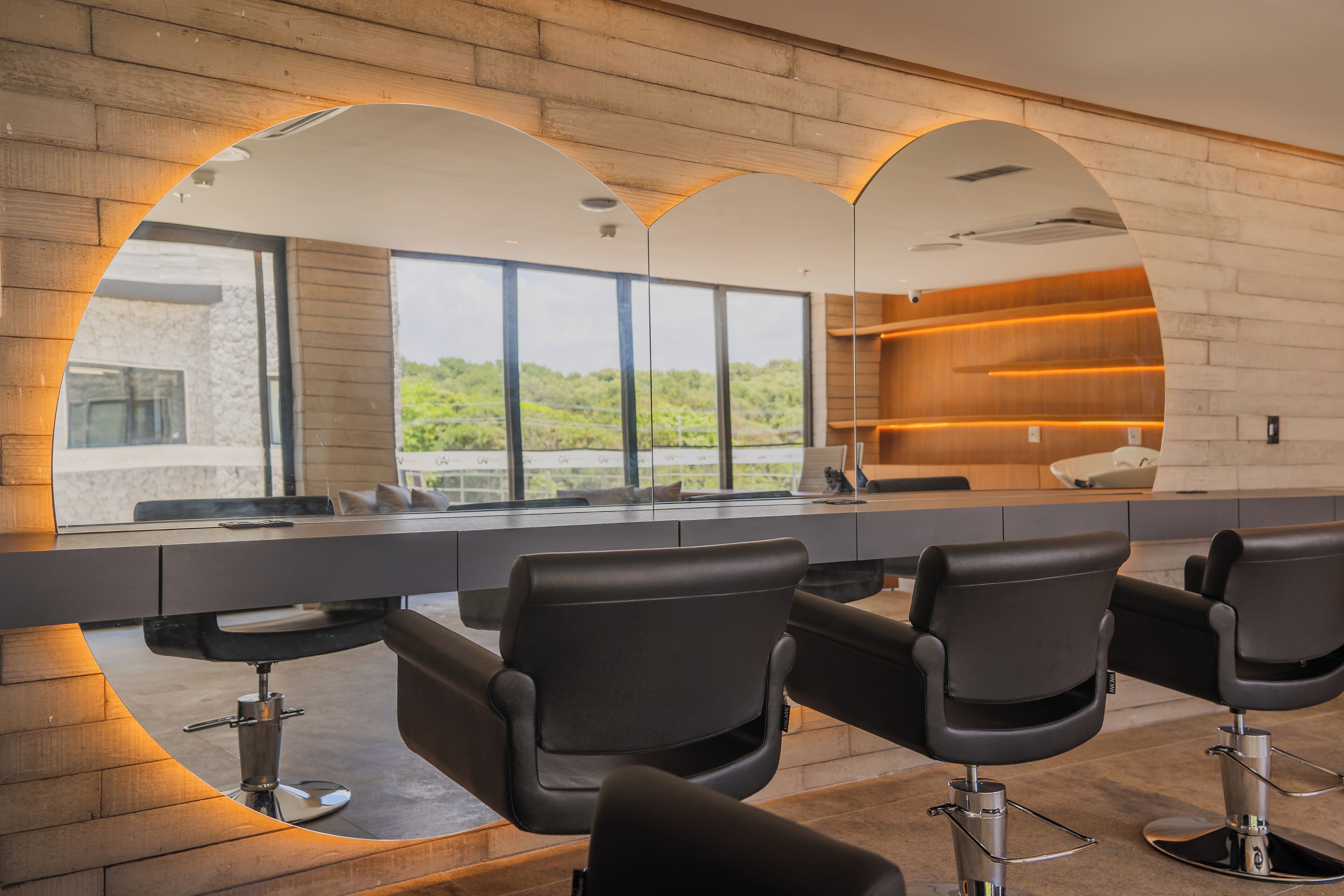 A modern hair salon with three black salon chairs, large windows, and a wooden interior.
