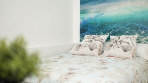 A bedroom with a bed featuring a floral and seashell pattern, two pillows with butterfly designs, and a wall mural of a wave. - Estudio en La Jaca, a 3 Minutos de la Playa, en un Lugar Ideal Para Desconectar (La Jaca)