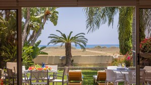 A patio with a table and chairs, a palm tree, and a view of the beach. - Larnaca Chelidonia Seafront Villa (Meneou)