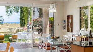 A modern kitchen with a glass dining table, white chairs, and a view of the sea. - Larnaca Chelidonia Seafront Villa (Meneou)