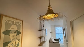 A hallway with a large poster, a unique hanging light fixture, and a view into a living area with a bicycle.
