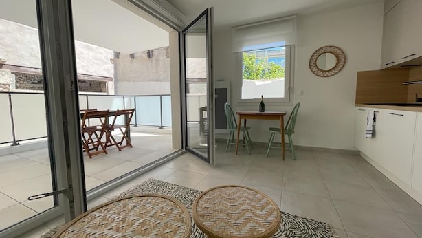 A modern apartment with a balcony, a dining area with a table and chairs, and a kitchen with cabinets and a window.
