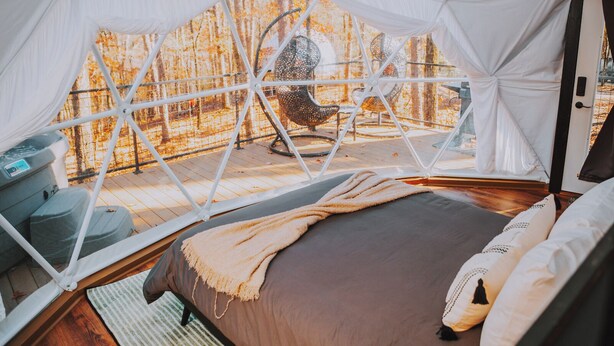 Habitación con tienda de campaña, cama, una silla y vista a árboles.