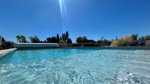 Une piscine d’un bleu éclatant, bordée de blanc, entourée d’arbres et surplombée d’un ciel dégagé.