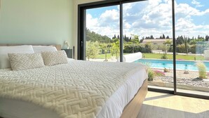 Une chambre avec un grand lit, une vue sur une piscine et un luminaire au plafond.