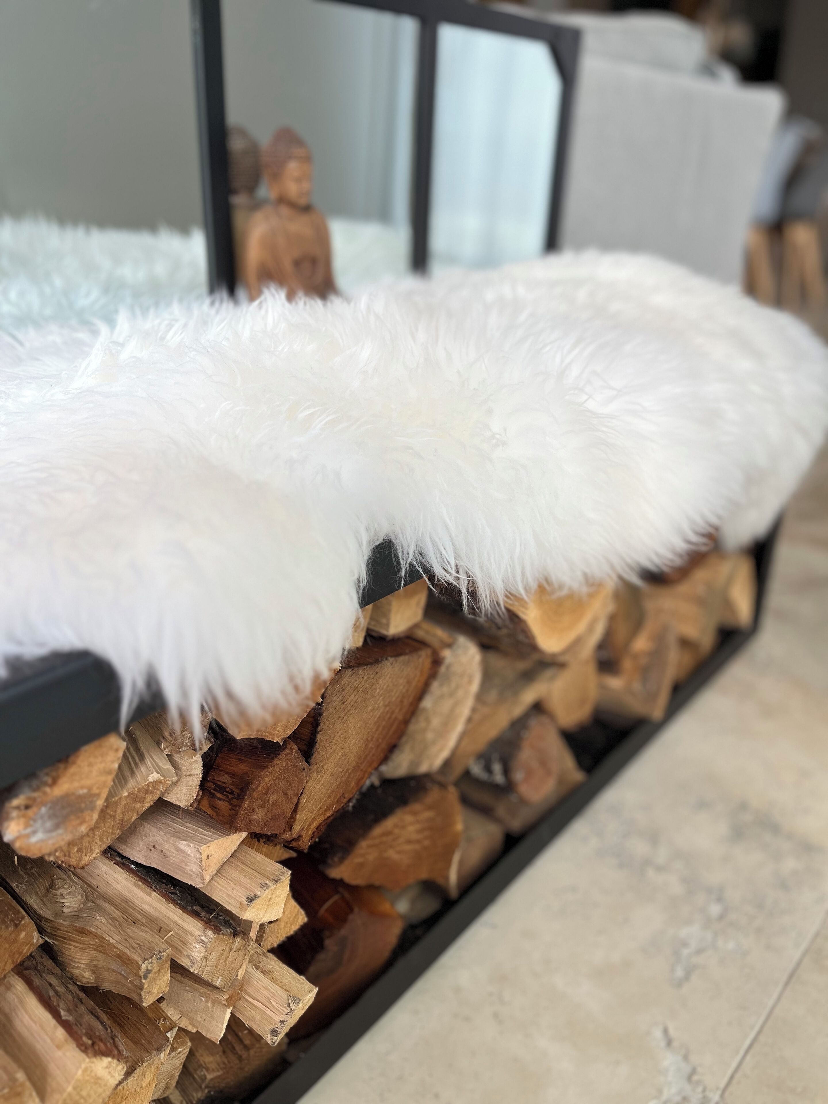 A close-up of a white fluffy object, possibly a cushion or blanket, resting on a stack of wood logs.