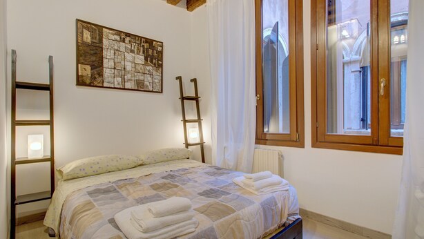 Un dormitorio con cama, una escalera de madera, una ventana con cortinas y un radiador.