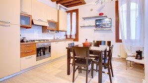 Una cocina moderna con vigas de madera, un comedor con mesa y sillas, y un horno empotrado.