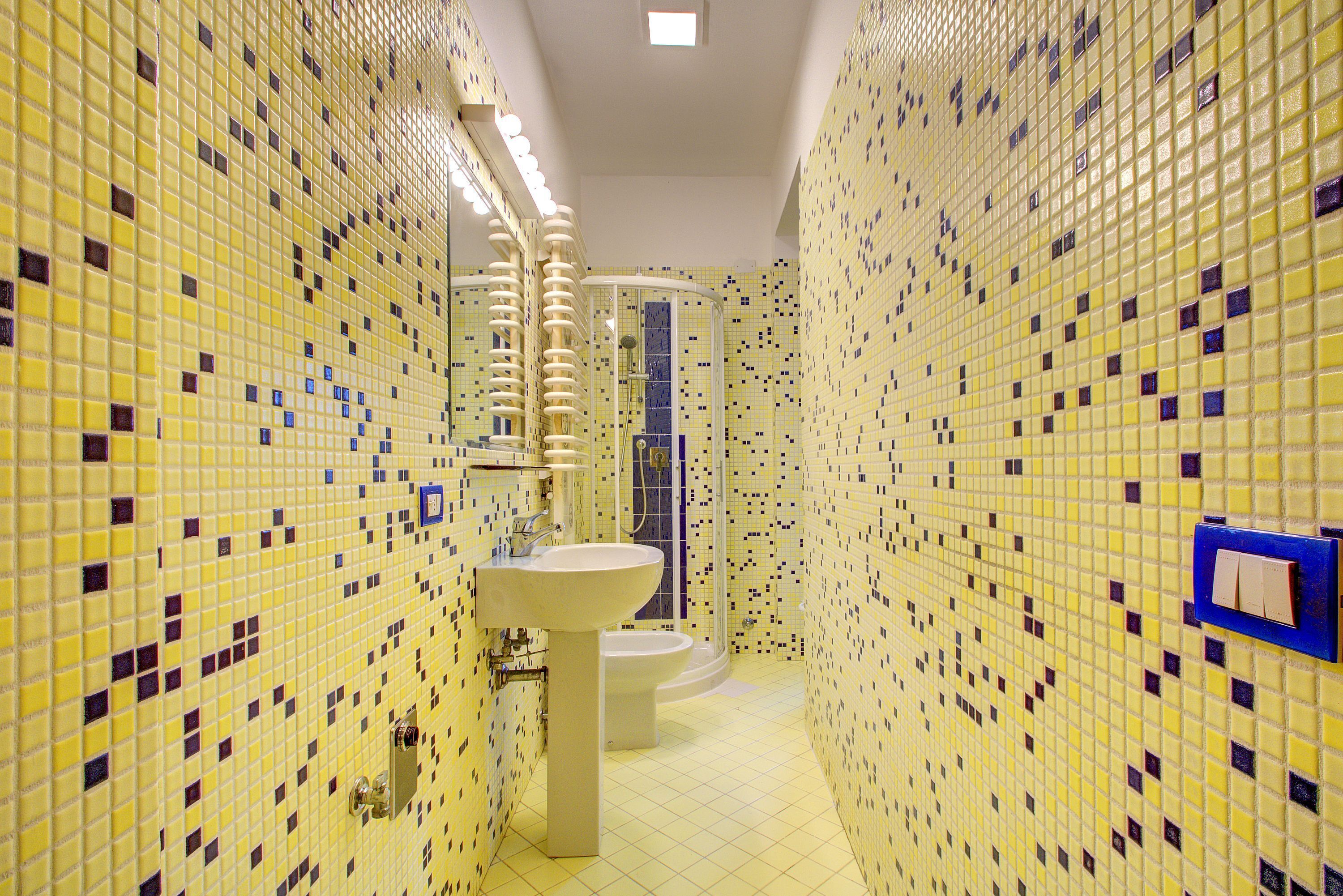 Ein Badezimmer mit gelben Mosaikfliesen, einem Waschbecken und einer Toilette.