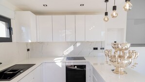 Une cuisine moderne avec des meubles blancs, un four encastré et un plan de travail agrémenté d’un saladier en verre et de verres à vin.