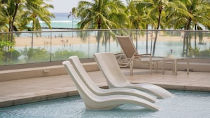 Ein Poolbereich mit Liegestühlen und Blick auf Strand und Meer.