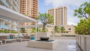 Eine Dachterrasse mit Außenmöbeln, einer zentralen Wasserspiele und Hochhäusern im Hintergrund.