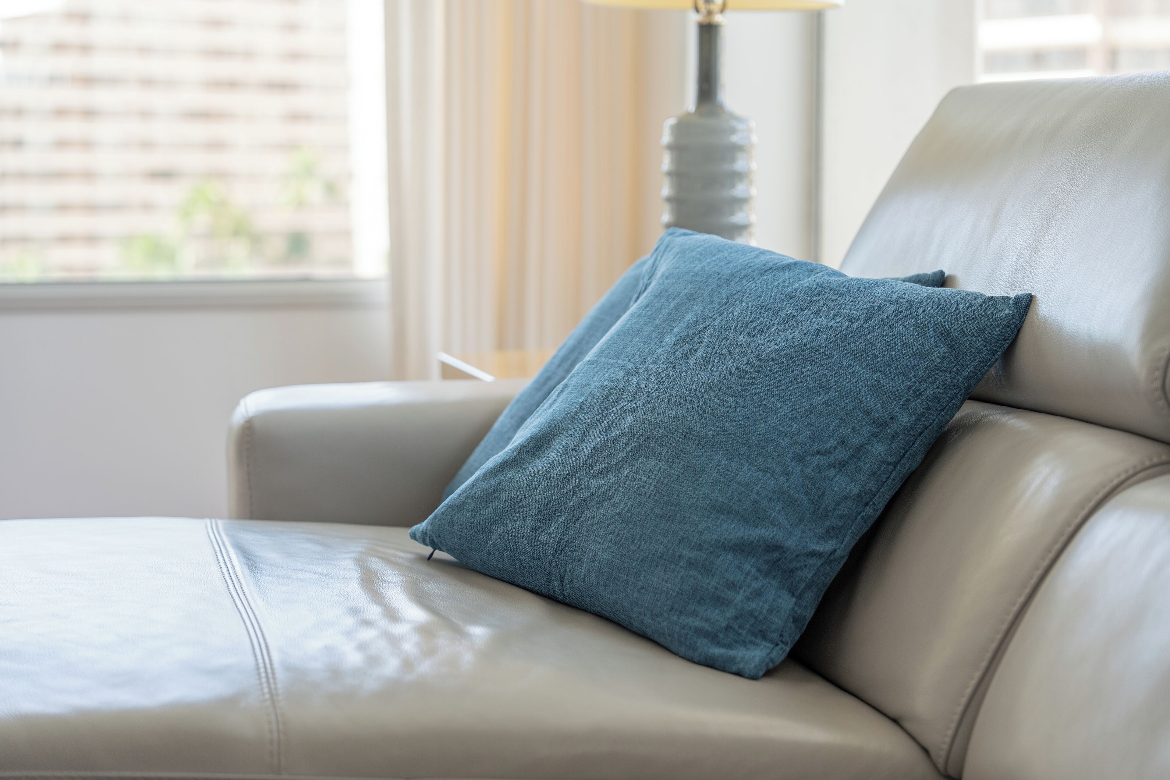A beige leather sofa with a single blue pillow.