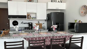 A modern kitchen with white cabinets, a black refrigerator, and a dining area with a patterned tablecloth. - Carrizo apartment (Mazatlán)
