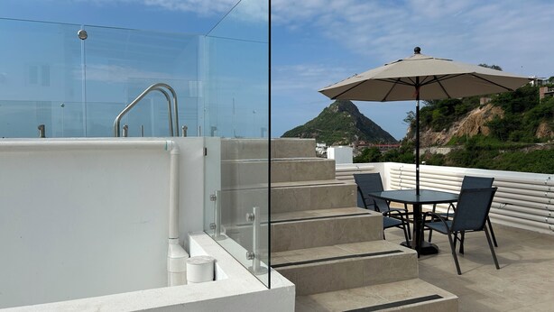 A rooftop terrace with a glass balustrade, outdoor seating, and a view of a mountain. - Carrizo apartment (Mazatlán)