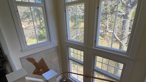 A wooden staircase with a metal handrail leading to a landing with large windows offering views of trees and a clear sky. - Summer House in Swedish Archipelago (Stockholms län)