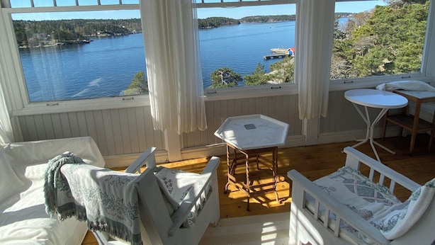 A cozy room with a large window overlooking a lake, furnished with white chairs and a small table. - Summer House in Swedish Archipelago (Stockholms län)