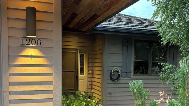 A house with a wooden exterior, a number '1206' sign, a door, and a small garden with plants and a rock border. - Townhouse in beautiful North Helena Valley, below the majestic Sleeping Giant (Helena)