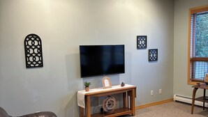 A living room with a flat-screen TV, leather sofas, a wooden coffee table, decorative wall art, and a window with blinds. - Townhouse in beautiful North Helena Valley, below the majestic Sleeping Giant (Helena)