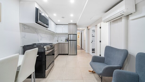 A modern kitchen with white cabinets, a built-in oven, and a microwave. There are two grey chairs and a dining table. - 16 shower Head Stay Luxury Stay (Passaic)