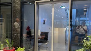 A modern building entrance with glass doors, a seating area with a desk and chair, and potted plants. - Riverside rooms at Hotel Fieri (Fier)