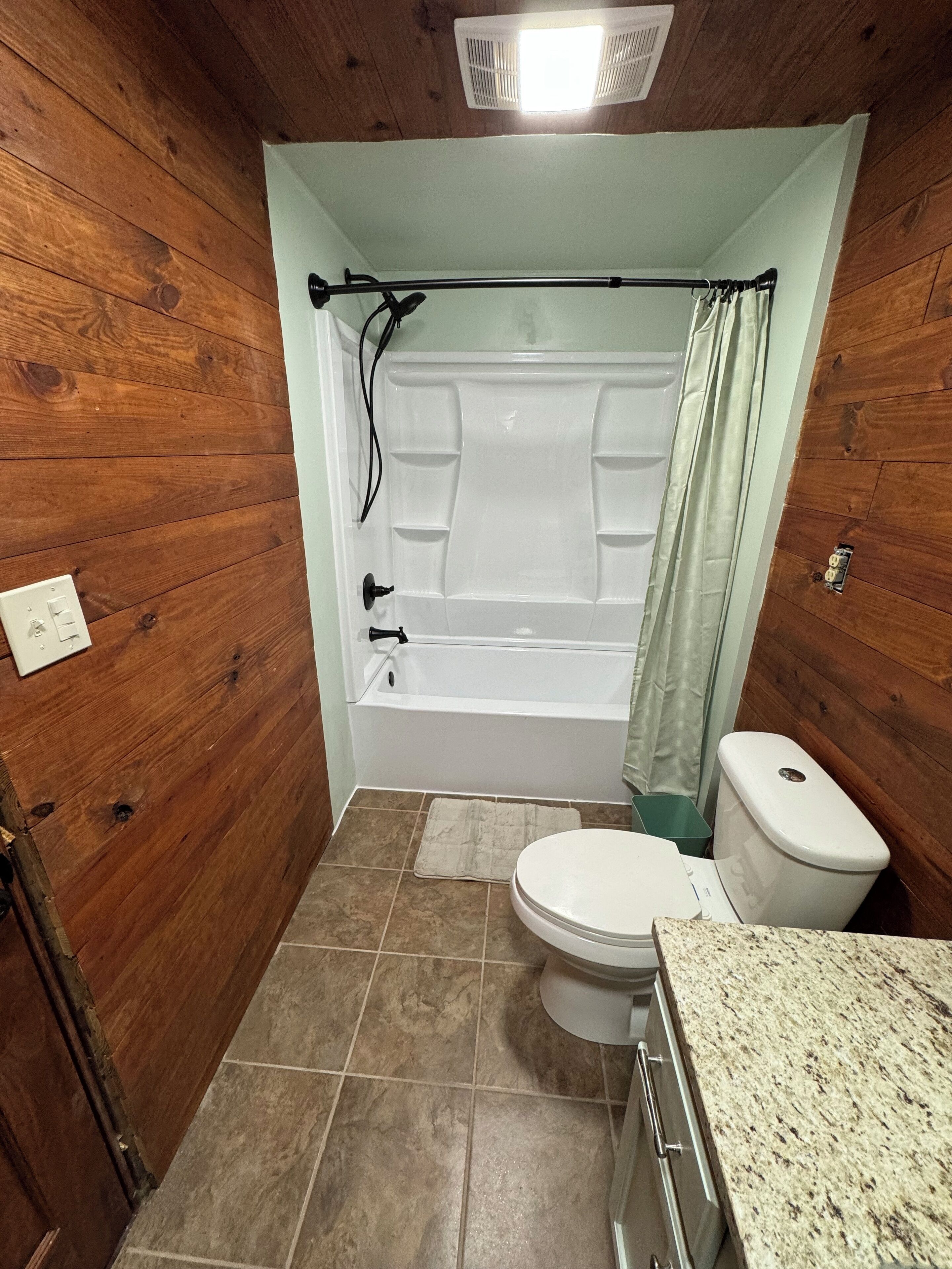 A bathroom with a wooden interior, a bathtub, a toilet, and a granite countertop.