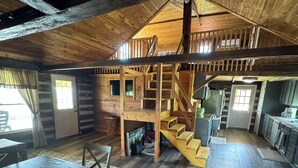 Interior rústico de una cabaña con una escalera de madera que conduce a un altillo, un comedor y una cocina.