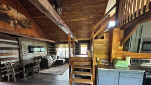 Interior rústico de una cabaña con una mesa de comedor de madera, sofá y área de cocina que incluye un microondas y armarios.