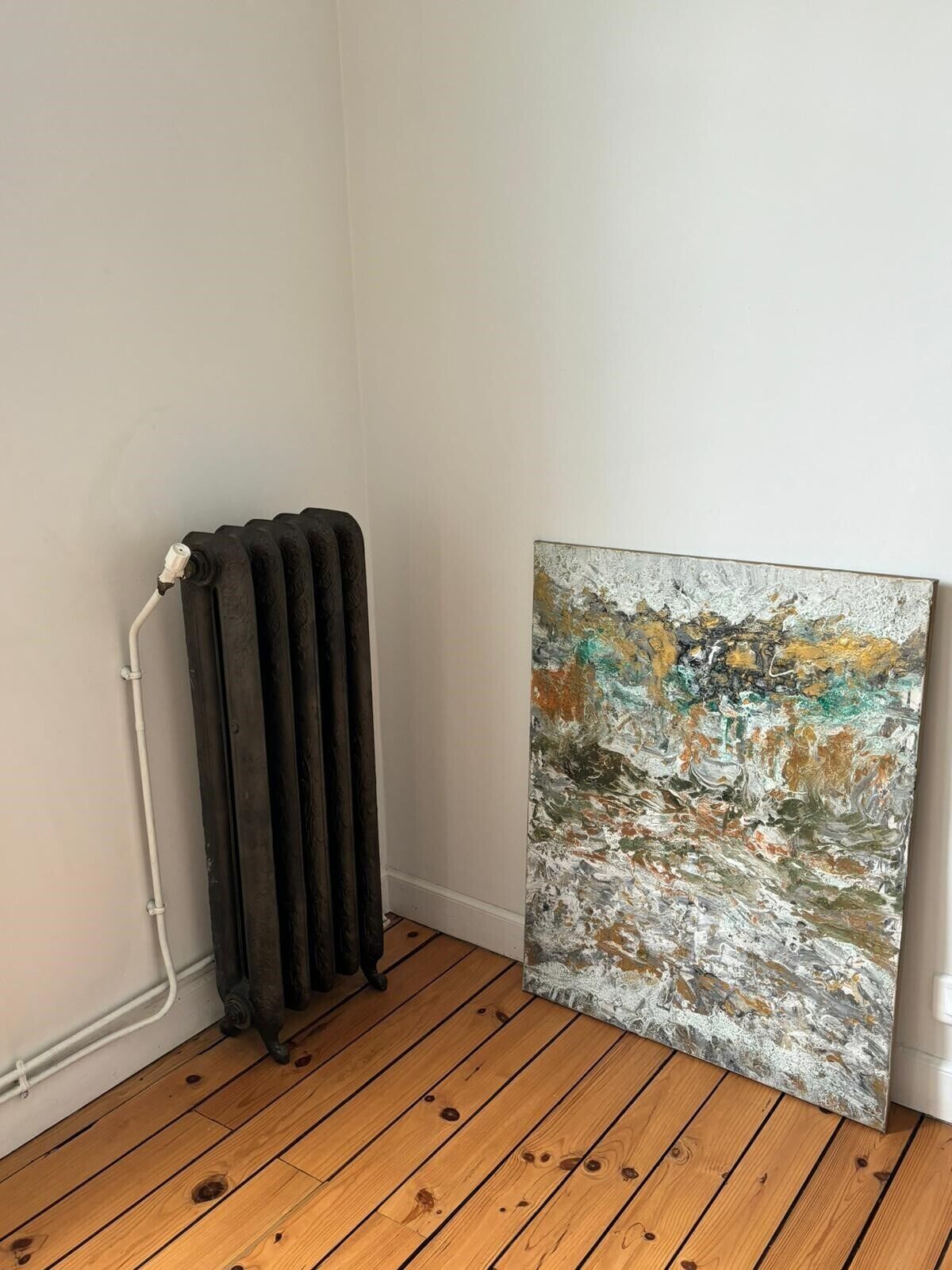 A room with a radiator, a wooden floor, and a large abstract painting on the wall.