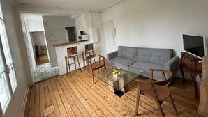Un salon moderne avec un canapé gris, des chaises en bois, une table basse en verre et un téléviseur.