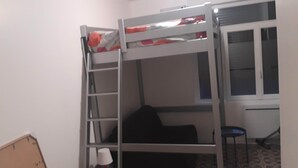 Una cama individual con escalera, una mesita y una silla en una habitación con ventana.