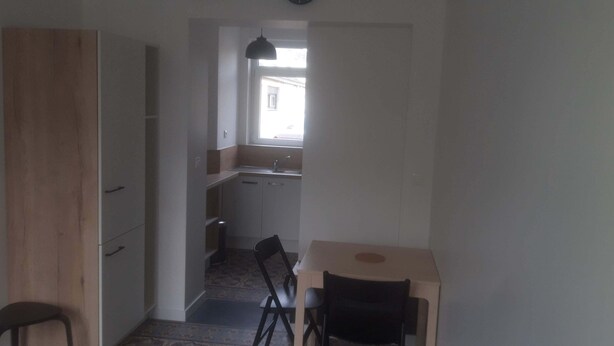 Un pasillo estrecho que da a una cocina con ventana, una mesita y una silla.