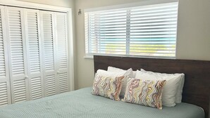 Un dormitorio con cama, contraventanas blancas y ventana con persianas.