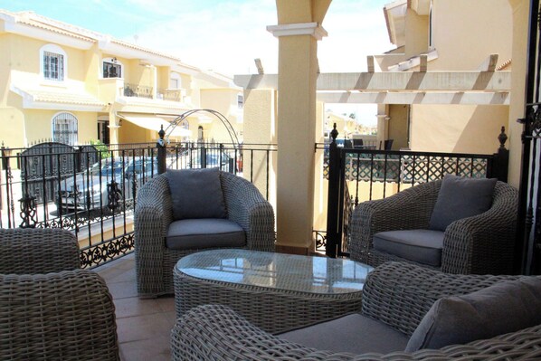 A balcony with wicker furniture, a glass table, and a view of neighboring buildings.