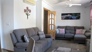 Ein Wohnzimmer mit zwei grauen Sofas, einem Glastisch, einem gemusterten Teppich und einer Holztür.