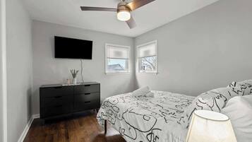 A bedroom with a bed, a ceiling fan, a TV mounted on the wall, and a dresser.