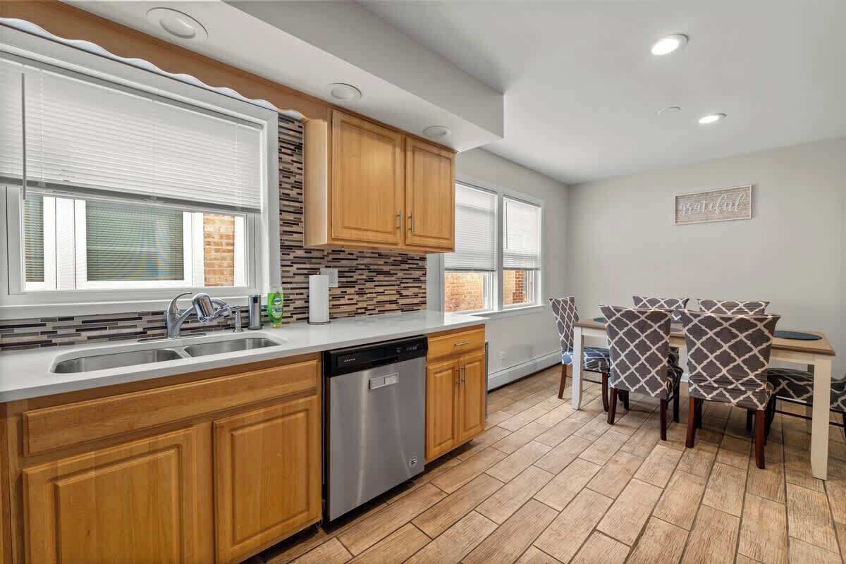 A modern kitchen with wooden cabinets, a dishwasher, and a dining area with patterned chairs.
