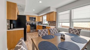 A modern kitchen with wooden cabinets, a black refrigerator, and a dining area with a table and chairs. - Cozy, Sunny, and Clean Apt 3 bd Free Parking (Berwyn)