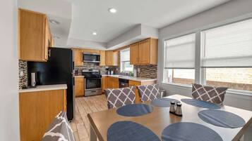 A modern kitchen with wooden cabinets, a black refrigerator, and a dining area with a table and chairs.