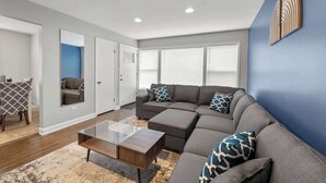 A modern living room with a sectional sofa, a glass coffee table, and a patterned rug. - Cozy, Sunny, and Clean Apt 3 bd Free Parking (Berwyn)
