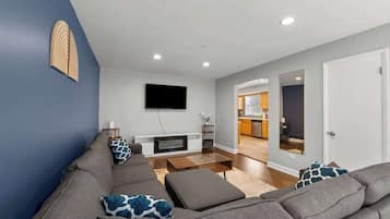 A modern living room with a grey sofa, a flat-screen TV mounted on the wall, and a wooden coffee table.