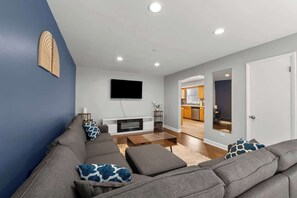 A modern living room with a grey sofa, a flat-screen TV mounted on the wall, and a wooden coffee table. - Cozy, Sunny, and Clean Apt 3 bd Free Parking (Berwyn)