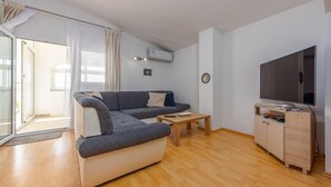 Ein modernes Wohnzimmer mit einem grauen Sofa, einem Holztisch und einem Fernseher auf einem Holzgestell.