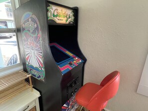 A vintage arcade machine with a colorful design and a red chair in front.