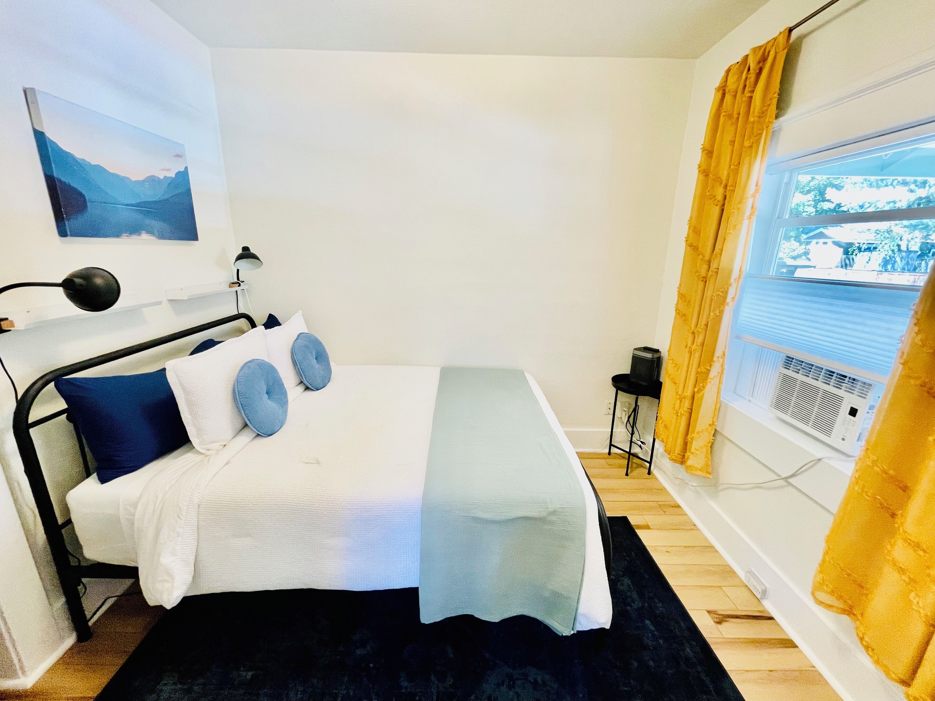 Una camera da letto ordinata con un letto, una lampada da comodino, un piccolo tavolo e una finestra con tende.