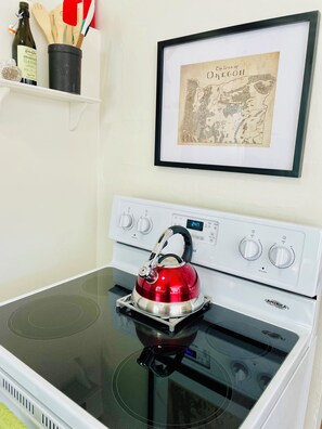 A kitchen with a stove, a kettle, and a framed map on the wall.
